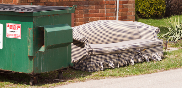 old couch sitting next to a dumpster