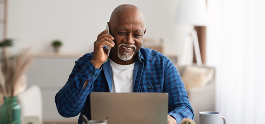 Man smiling on the phone in front of laptop