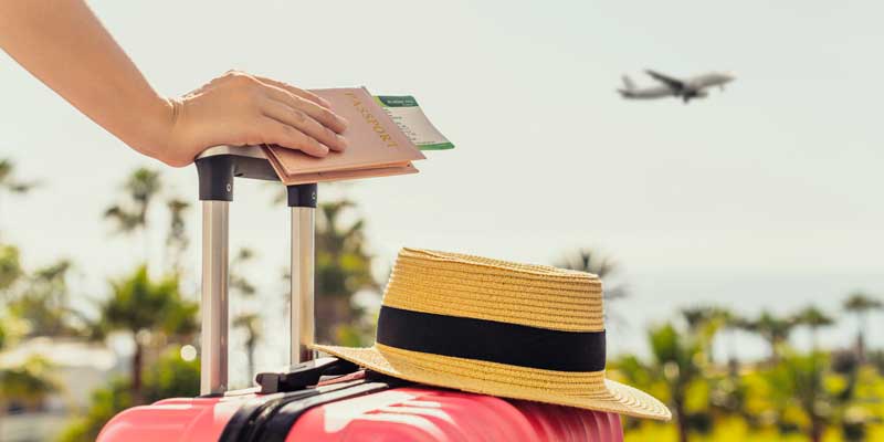 person with suitcase and passport watching plane take off