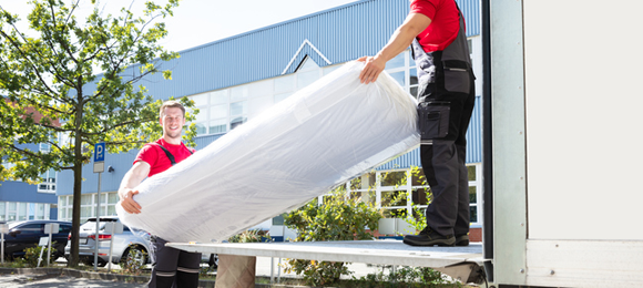 two junk removal workers loading mattress into hauling vehicle