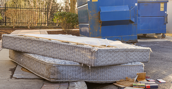 Two old mattresses next to a commercial dumpster