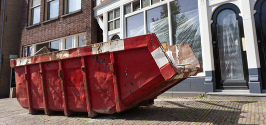 Red roll-off dumpster on city sidewalk in front of apartment building