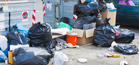 piles of garbage and trash outside of overflowing garbage bin