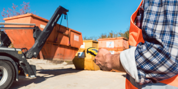 Dump truck driver loading roll-off dumpster onto a dump truck